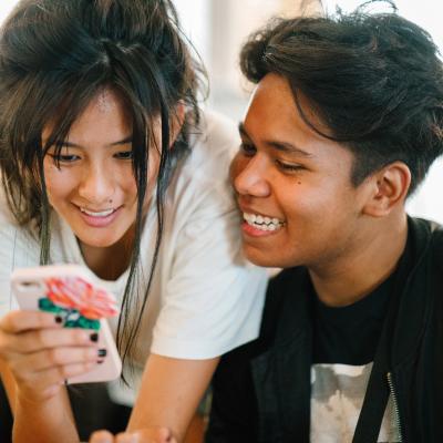 Two adolescents (a boy and a girl) playing on the girl's cell phone
