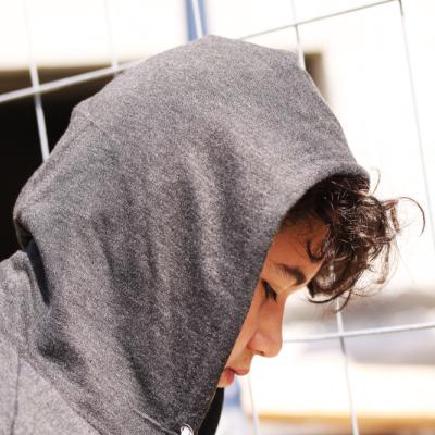 Young adolescent boy in a grey hoodie sadly looking down at the ground