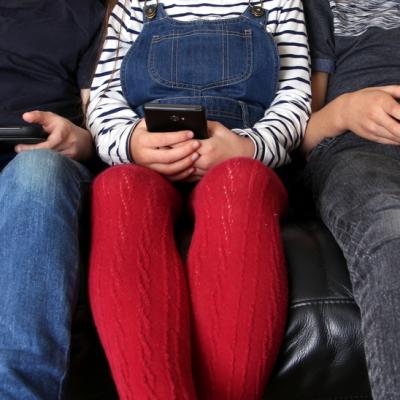 Three children playing on a tablet, mobile phone, and video game console