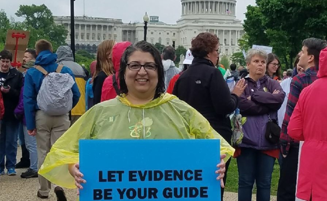 SRCD Executive Director, Laura L. Namy, at March for Science in Washington, D.C., holding sign that says "Let Evidence Be Your Guide" in front of the U.S. Capitol Building