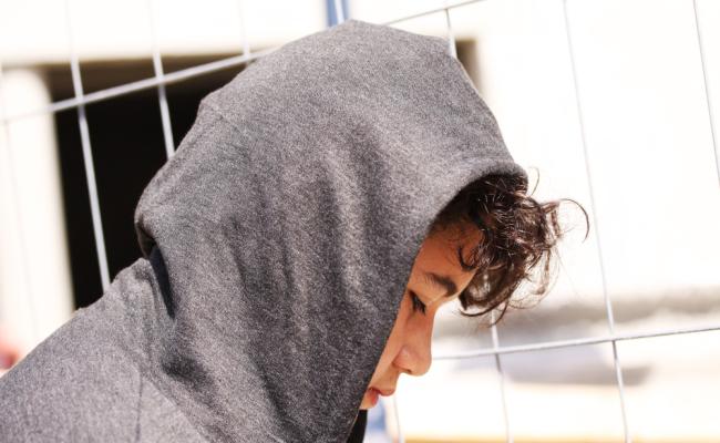 Young adolescent boy in a grey hoodie sadly looking down at the ground